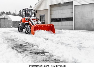 Little red tractor with snowplow in a motion removing snow . Reduced visibility in  snow flurries.