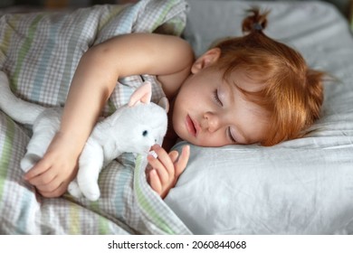 a little red-haired girl sleeps peacefully at night in her bed and hugs a plush kitten.  - Powered by Shutterstock