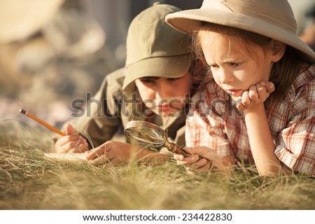 Little researchers - boy and girl - study of insects and plants, crawling on his stomach on the grass in a sunny summer day