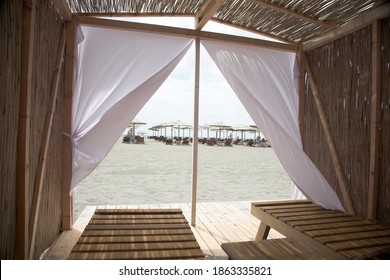 Little Resting Hut Interior With White Curtain And Wooden Benches At Sandy Beach.