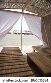 Little Resting Hut Interior With White Curtain And Wooden Benches At Sandy Beach.