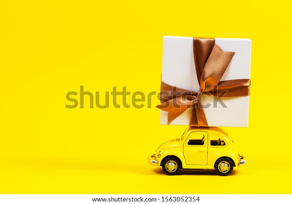 Little retro toy model car with present gift box\
on yellow background. Christmas, birthday, valentines day, delivery\
concept