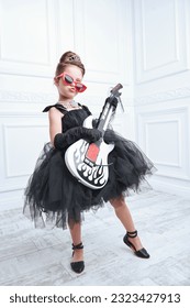 Little rock star. A funny pretty girl in a magnificent evening dress and with an elegant evening hairstyle plays the electric guitar and sings.