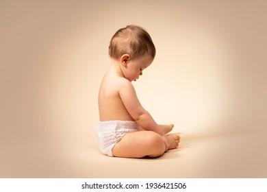 Little Sad Baby Toddler, Alone Child. Sitting On A Plain Background In Diaper.