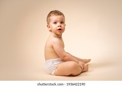 Little Sad Baby Toddler Sitting On A Plain Background In Diaper. Surprised Child.