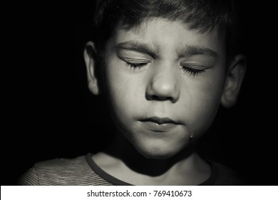 Little sad boy crying on black background. Abuse of children concept