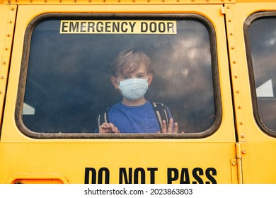 Little Sad Boy Kid Student In Protective Face Mask Looking Out Of School Yellow Bus Window. New Normal At Coronavirus Covid-19 Pandemic. Measurements Against Virus Spread In Class.
