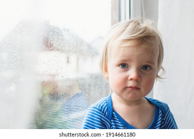 Little Sad Boy Sitting At Home On Window In Rainy Day. Stay Home Coronavirus Concept.