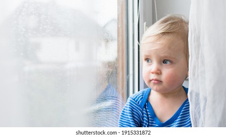 Little Sad Boy Sitting At Home On Window In Rainy Day. Stay Home Coronavirus Concept.