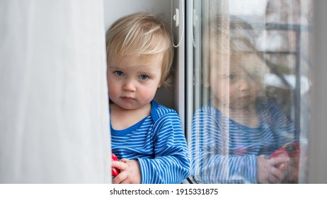 Little Sad Boy Sitting At Home On Window In Rainy Day. Stay Home Coronavirus Concept.