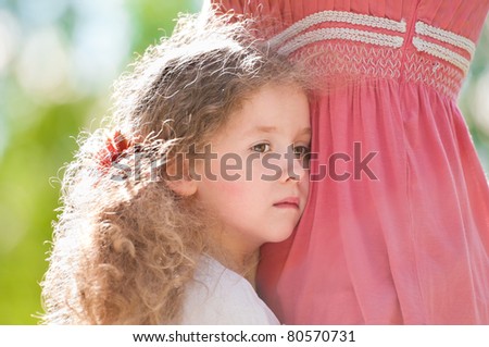Little sad daughter hugging her mother. Nature background.