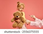 Little sad girl, child holding teddy bear toy while doctor holding syringe and making vaccination against pink studio background. Concept of healthcare, medical treatment, vaccination, childhood