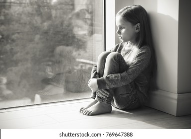 Little sad girl near window. Abuse of children concept