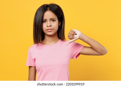 Little Sad Kid Girl Of African American Ethnicity 12-13 Years Old In Pink T-shirt Showing Thumb Down Dislike Gesture Isolated On Plain Yellow Background Studio Portrait. Childhood Lifestyle Concept