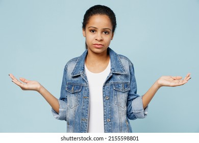 Little Sad Kid Teen Girl Of African American Ethnicity 12-13 Years Old In Denim Jacket Shrugging Shoulders Have No Idea Spread Hands Isolated On Pastel Plain Light Blue Background. Childhood Concept