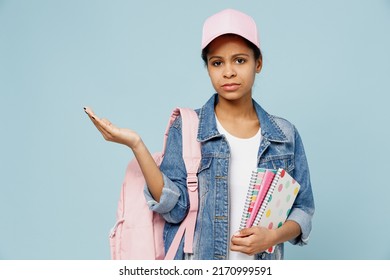 Little Sad Schoolgirl Kid Teen Girl Of African American Ethnicity 12-13 Year Old In Denim Jacket Backpack Cap Hold Exercise Books Notebooks Spread Hand Isolated On Pastel Plain Light Blue Background