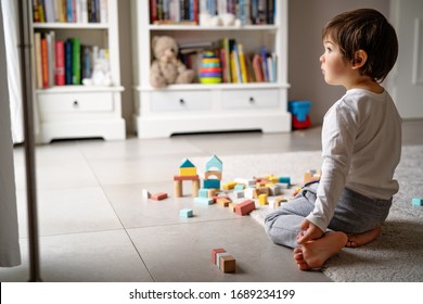 Little Sad Thoughtful Bored Toddler Boy Playing Wooden Colorful Building Blocks Alone At Home During Quarantine Looking At Window. Development Game. Loneliness At Self Isolation Period