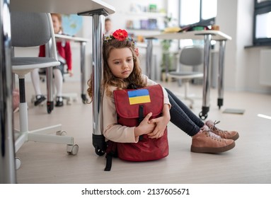 Little sad Ukrainian girl sitting on floor at school, concept of enrolling Ukrainian kids to schools. - Shutterstock ID 2137605671