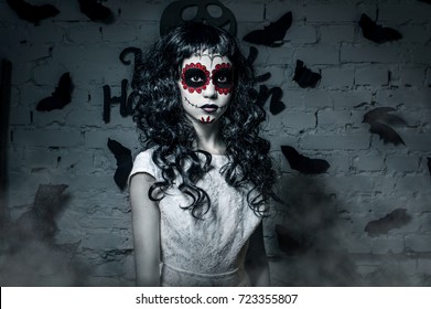Little santa muerte girl with black curly hair dressed in white as the halloween character
