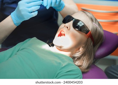 Little scared girl sitting in chair in dentist doctor office. Protective safety sunglasses. Kid,child afraid of tooth extraction, teeth treatment. Open mouth. Dental clinic check-up.Reclined position. - Powered by Shutterstock