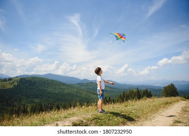 Little school age boy running down the slope with kite in the sun. Sunny summer or spring day at sunset. Active outdoor games and leisure. Mountain landscape with hills and coniferous trees. - Powered by Shutterstock