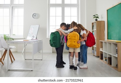 Little school friends develop social skills and support each other. Group of elementary students huddling in modern classroom interior . Several children standing in circle and hugging each other - Powered by Shutterstock