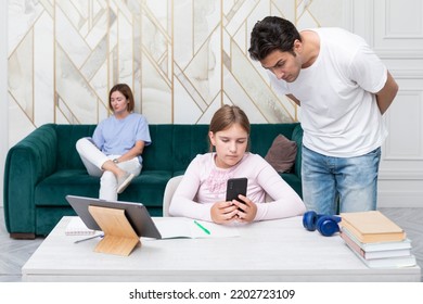 Little School Girl Studies At Home And Her Father Helps Her. Serious Dad Controls His Daughter While She Learning Lessons