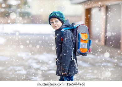 Little School Kid Boy Of Elementary Class Walking To School. Happy Child Having Fun And Playing With First Snow. Student With Backpack In Colorful Winter Clothes. School Building: