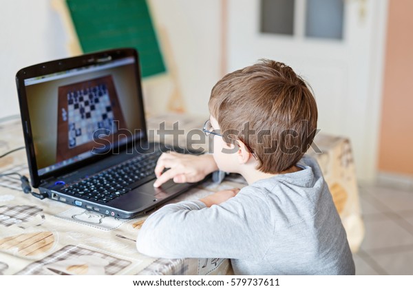 Little school kid boy with glasses playing\
online chess board game on computer. Child having fun with learning\
on pc. Education\
concept.