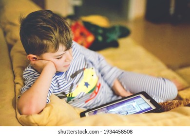 Little School Kid Boy Making Homework With Tablet. Schoolchild Reading And Learning With Computer, Searching For Information In Internet And Looking Cartoons Beforte Sleeping And Going To Bed.