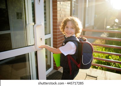 Der kleine Schuljunge öffnet eine Schultür. Der Junge ist hübsches Gesicht. Hinter dem Rucksack, in den Händen ein hellgrüner Ordner. Schoolboy schaut in die Kamera und lächelt.