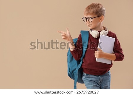 Little schoolboy with tablet computer pointing at something on beige background