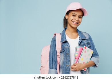 Little schoolgirl kid teen girl of African American ethnicity 12-13 year old in denim jacket backpack cap hold exercise books notebooks isolated on pastel plain light blue background Childhood concept - Shutterstock ID 2162727841