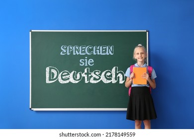 Little schoolgirl near blackboard with text SPRECHEN SIE DEUTSCH? (DO YOU SPEAK GERMAN?) in classroom