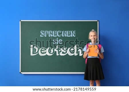 Little schoolgirl near blackboard with text SPRECHEN SIE DEUTSCH? (DO YOU SPEAK GERMAN?) in classroom