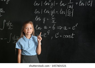 Little schoolgirl with raised index finger near blackboard