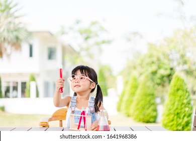 Little Scientist Asian Toddler Nerd Girl Wearing Glasses With Red Liquid Into Flask And Shaking.Home School Girl Learning About Science And Pouring Reagent Into Flask.Chemistry Class At Home.Nerd Kid.