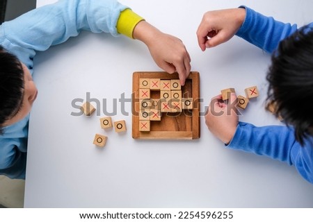 Little siblings playing wooden board game tic-tac-toe on table in living room. Family spending time together on weekend.