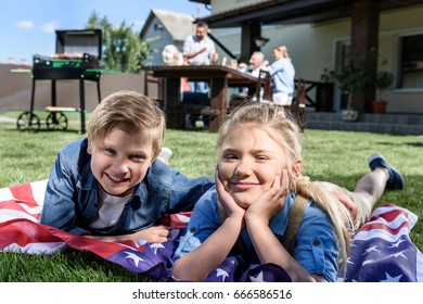 little siblings resting on american flag with family having picnic behind