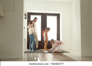 Little Sister Helping Brother To Tie Shoes, Girl Fasten Shoelaces Of Boy While Parents Looking At Kids Siblings Son And Daughter Helping Getting Ready For Walk Together Standing In Hallway At Home 