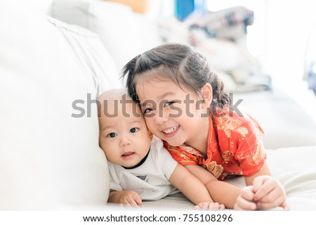 Little sister hugging her baby boy brother. Toddler kid meeting new sibling. Cute girl and new born baby boy relax in a sofa bed. Family with children at home. Love, trust and tenderness.