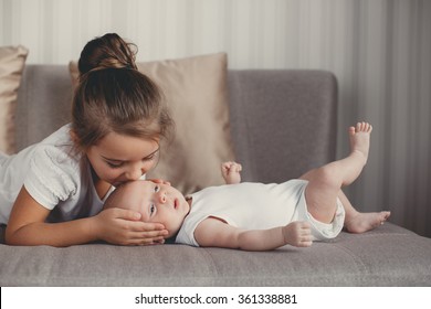 Little sister hugging her newborn brother. Toddler kid meeting new sibling. Cute girl and new born baby boy relax in a white bedroom. Family with children at home. Love, trust and tenderness