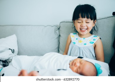 Little sister hugging her newborn brother. Toddler kid meeting new sibling. Cute girl and new born baby boy relax in a sofa. Family with children at home. Love, trust and tenderness