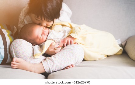 Little sister hugging and kissing her newborn brother.Toddler kid meeting new sibling. Cute girl and new born baby boy relax in a white bedroom.Family with children at home. Love, trust and tenderness