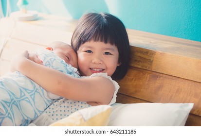 Little sister hugging and kissing her newborn brother.Toddler kid meeting new sibling. Cute girl and new born baby boy relax in a sofa.Family with children at home. Love, trust and tenderness.