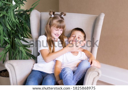 Little sister plays with her brother. Cute girl and boy are sitting at home.