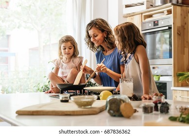Kleine Schwestern kochen mit ihrer Mutter in der Küche. Kinderkochkonzept.