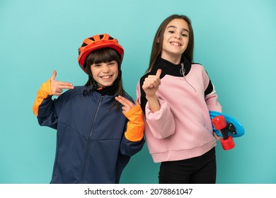 Little sisters practicing cycling and skater isolated on blue background proud and self-satisfied in love yourself concept