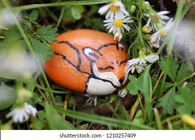 A little sleeping red fox is painted on a rock and hiding in the cozy grass and flowers in the garden.