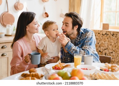 Little Small Caucasian Toddler Infant New Born Baby Eating Berry While Dad Father Feeding Child Kid. Young Family Of Three Having Morning Breakfast At Home Kitchen